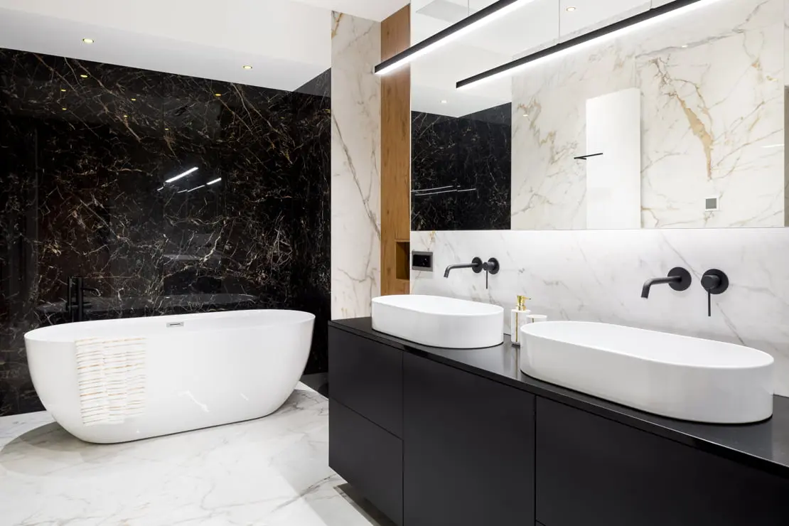 Luxusní koupelna s dvojitým umyvadlem, černými vestavěnými kohoutky a vanou na konci místnosti