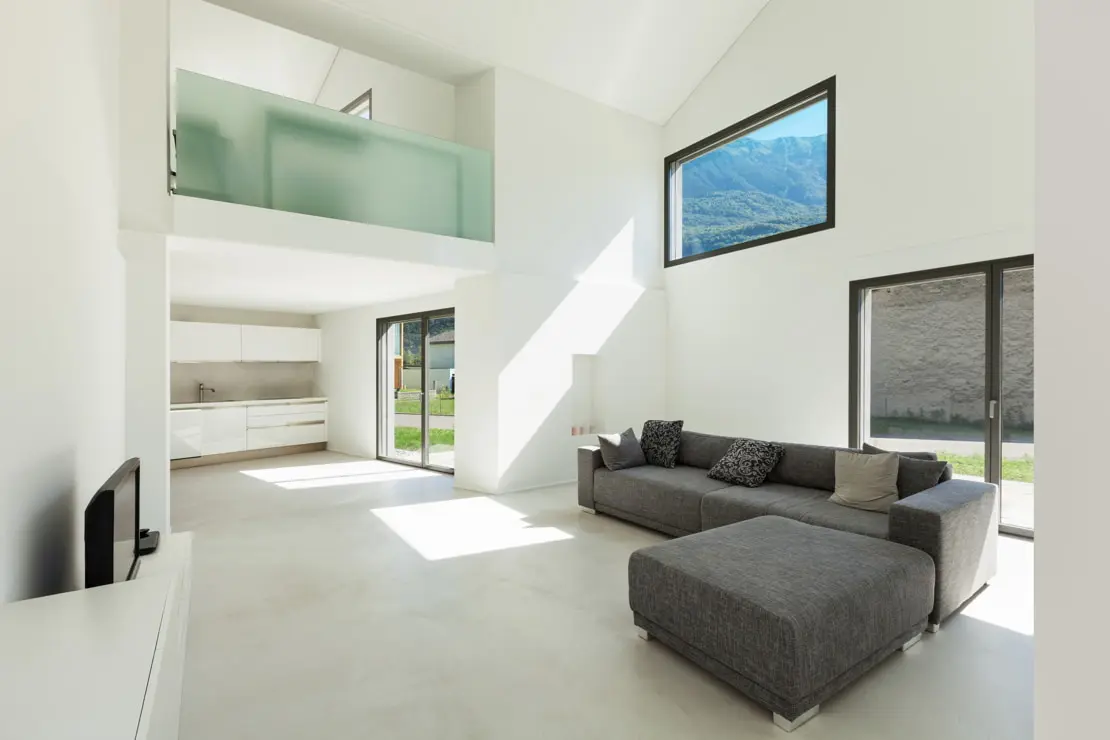 Microcement on the floor of a high-ceilinged living room that connects with the kitchen