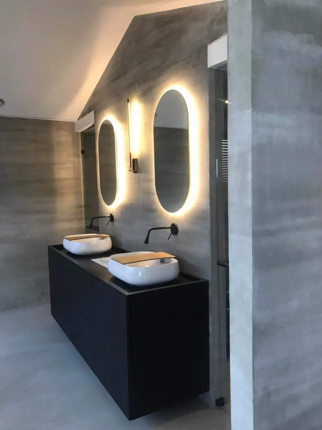 Béton ciré sur le sol et les murs d'une salle de bain minimaliste décorée avec des robinets noirs
